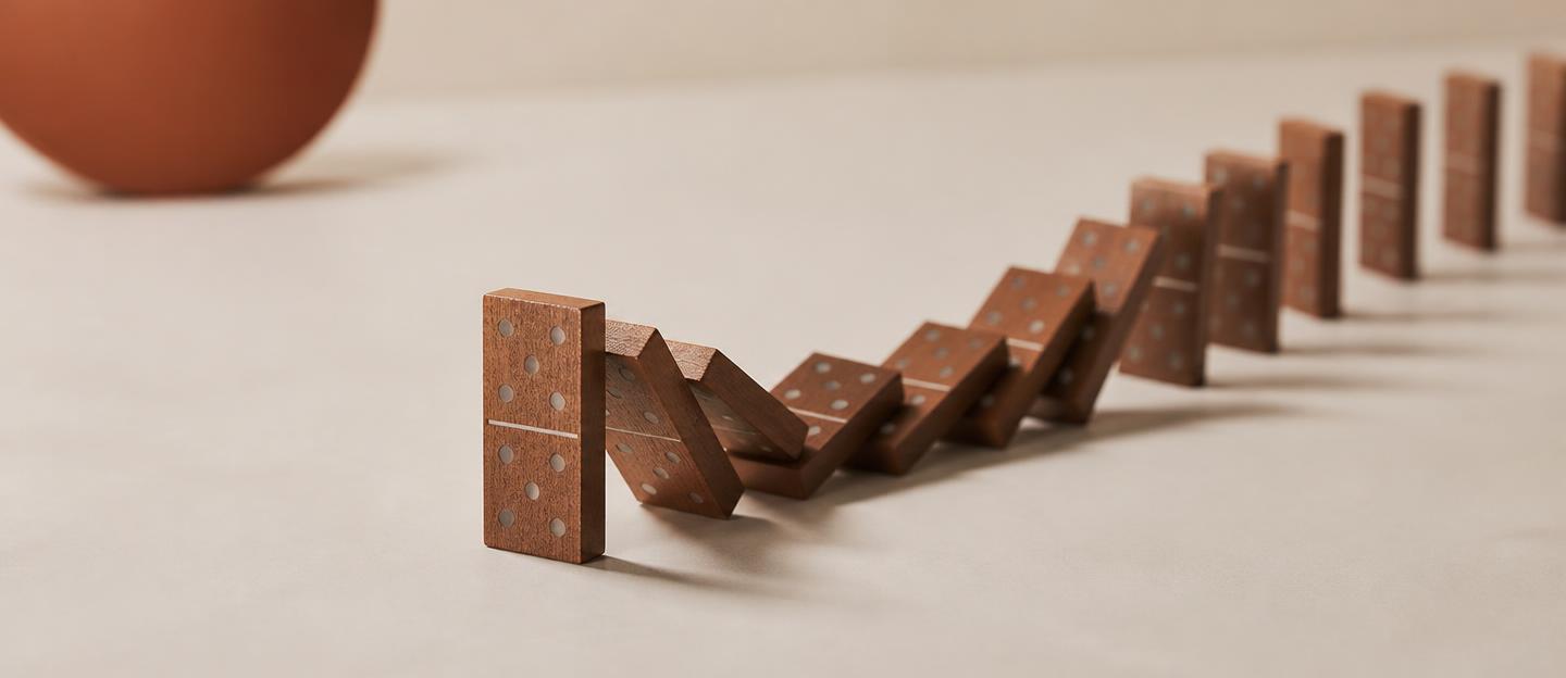 Een houten domino die een kettingreactie in beweging zet